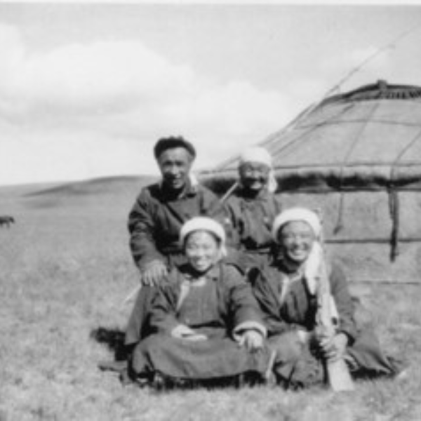 Black and white photo of a group of four Asian people sitting or standing outside a ger